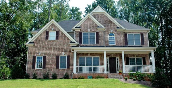 A large brick house with a porch and lawn.